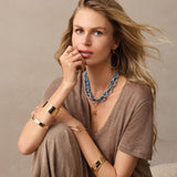 Woman wearing layered necklaces and bracelets on a neutral background