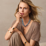 Woman wearing layered necklaces and bracelets on a neutral background